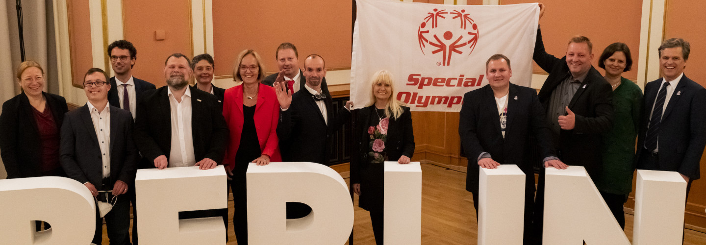 Special Olympics Athlet Robert Herberg nimmt die Special Olympics Fahne stellvertretend für alle Special Olympics Athlet*innen entgegen. Timothy Shriver, Chairman Special Olympics International, Ian Harper, Christiane Krajewski, Präsidentin Special Olympics Deutschland (SOD), Mark Solomeyer, Athletensprecher SOD, und Iris Spranger, Senatorin für Inneres, Digitalisierung und Sport, (von links nach rechts) reichen die Fahne beim Parlamentarischen Abend im Roten Rathaus am 28. April an Robert Herberg weiter.