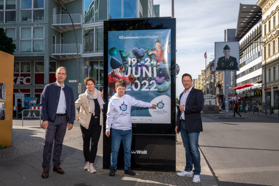 Patrick Möller (Geschäftsführer Wall GmbH), Frauke Bank (Leiterin Corporate Communications & Affairs Wall GmbH), Arthur Hackenthal (Organisationskomitee der Special Olympics World Games Berlin 2023) und Albert Tuemann (CMO Special Olympics World Games Berlin 2023) positionieren sich an der Berliner Friedrichstraße Ecke Zimmerstraße zum Start der Eventkampagne der Special Olympics Nationalen Spiele Berlin 2022 vor einem der ersten gehängten Motive (v.l.n.r.)